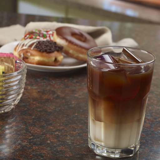 Iced coffee with crescent ice cubes next to a plate of assorted donuts on a brown countertop.