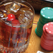 Drink with ice cubes and cherries beside poker chips on a wooden table.